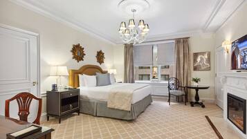 A hotel room with a bed, bedside table, lamp, chair, fireplace, and a window with curtains.