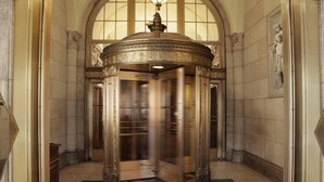 A grand, ornate elevator with a circular design and a decorative top, situated in a hallway with tiled walls and a marble floor. - The Sherry Netherland (New York)
