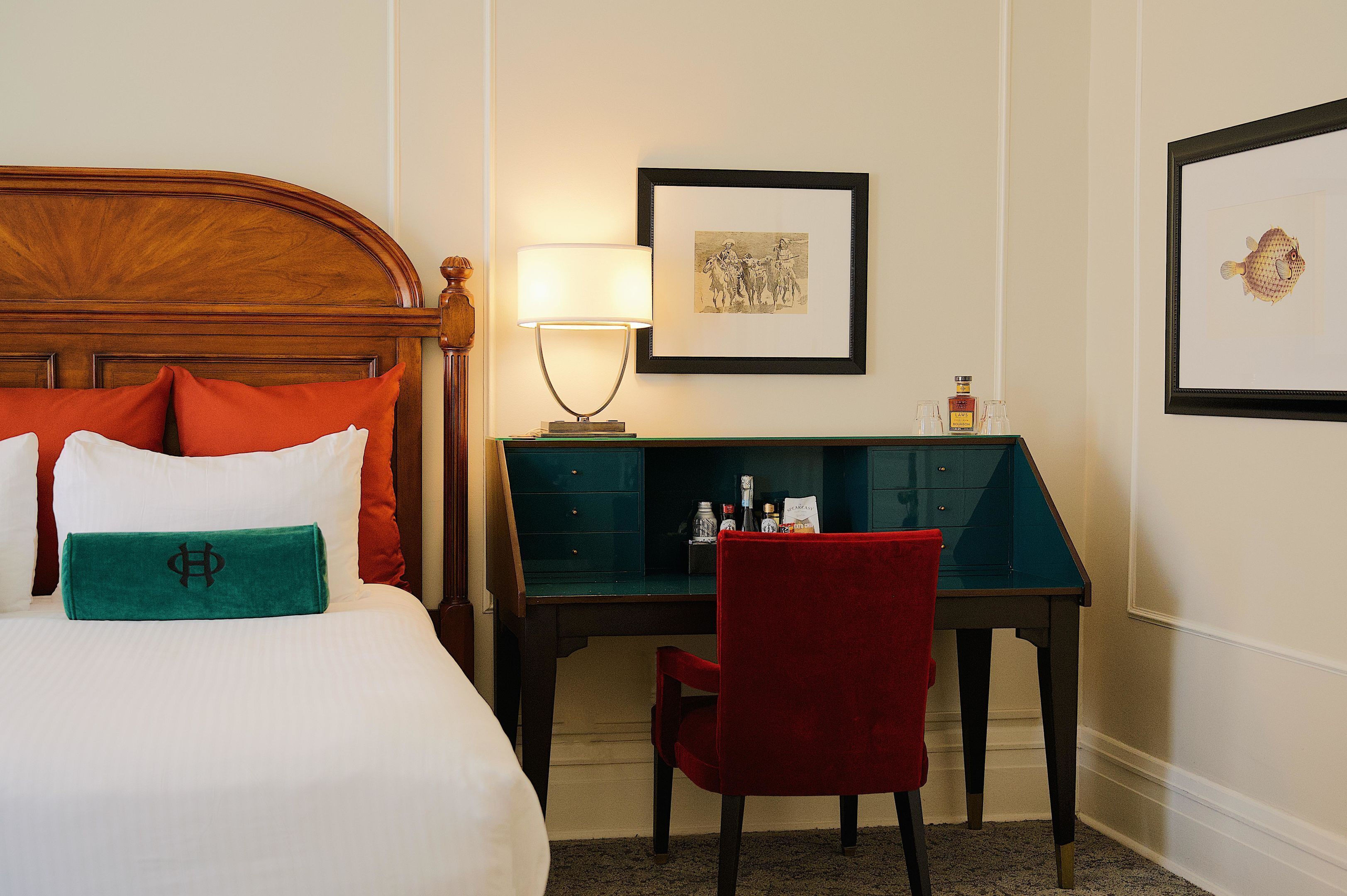 Une chambre d’hôtel équipée d’un lit, d’un bureau, d’une chaise, d’une lampe, de tableaux encadrés et d’un mini-bar.