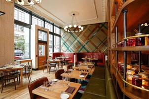 Un interior de restaurante con mesas de madera, asientos tipo cabina rojos y una zona de bar con frascos.