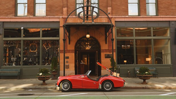 A red convertible parked in front of a building with large windows and a decorative entrance. - The Oxford Hotel (Denver)