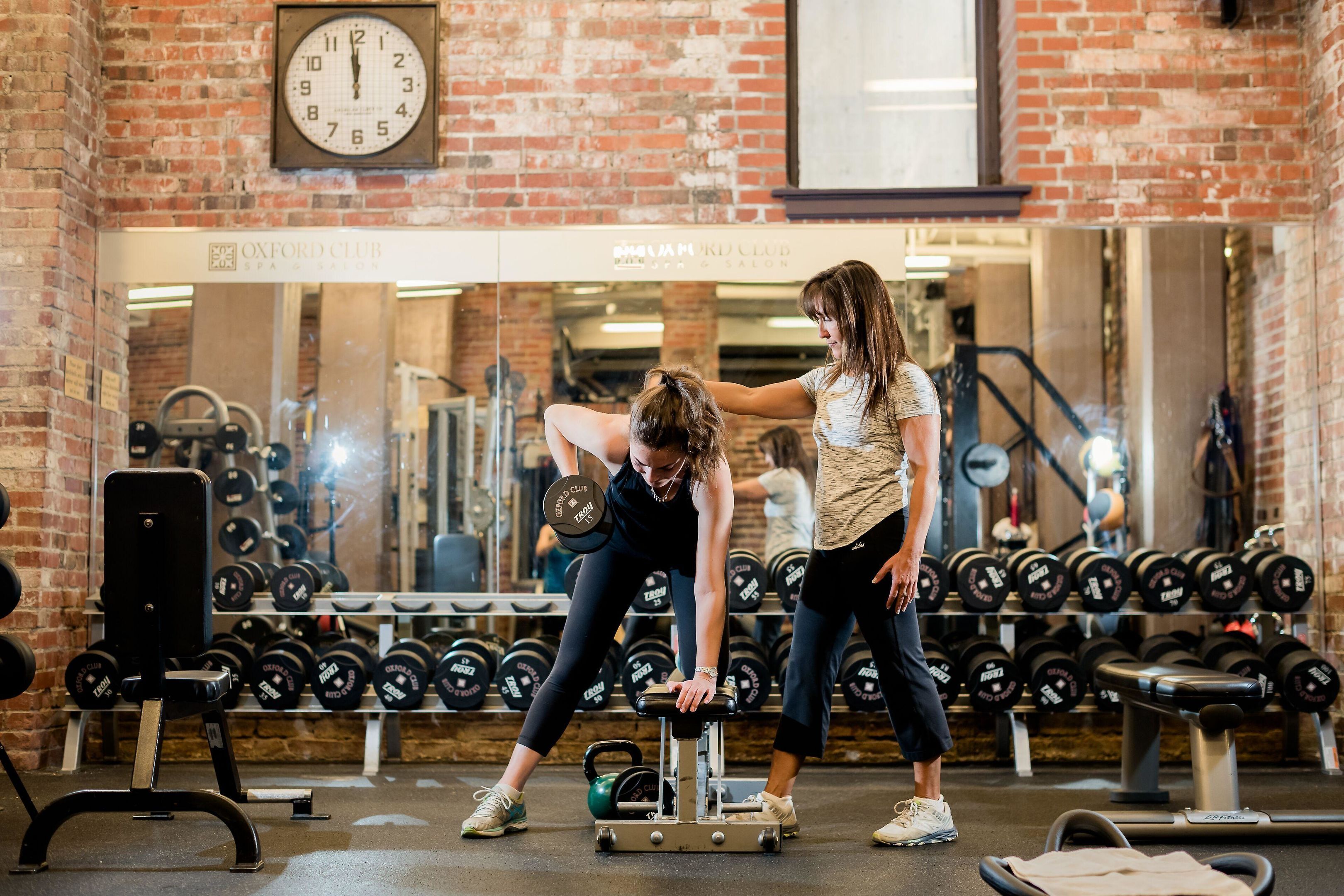 Une salle de sport équipée de matériel de musculation, avec une horloge et un miroir qui reflète l’espace.