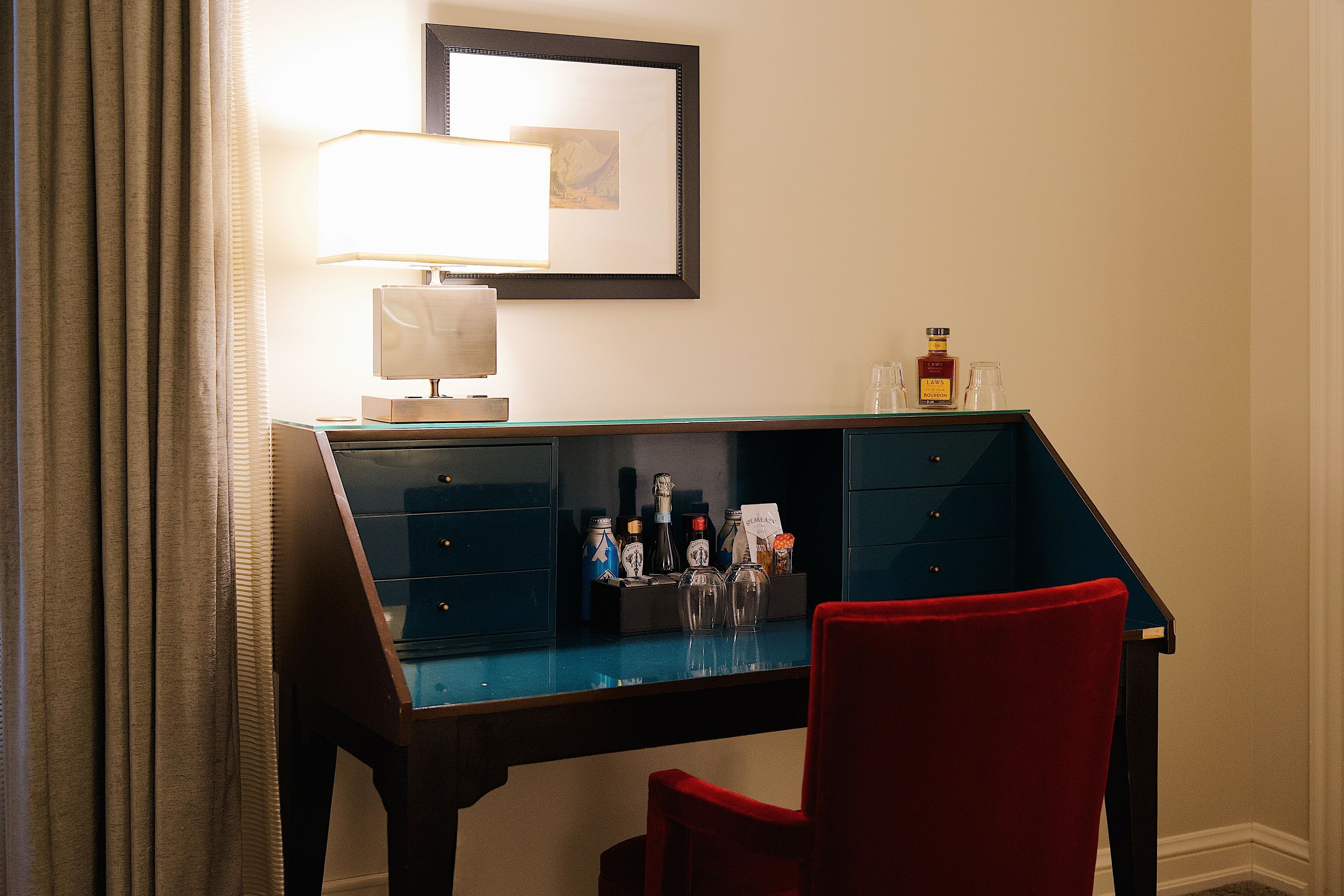A desk with a lamp, a chair, and a display of bottles.