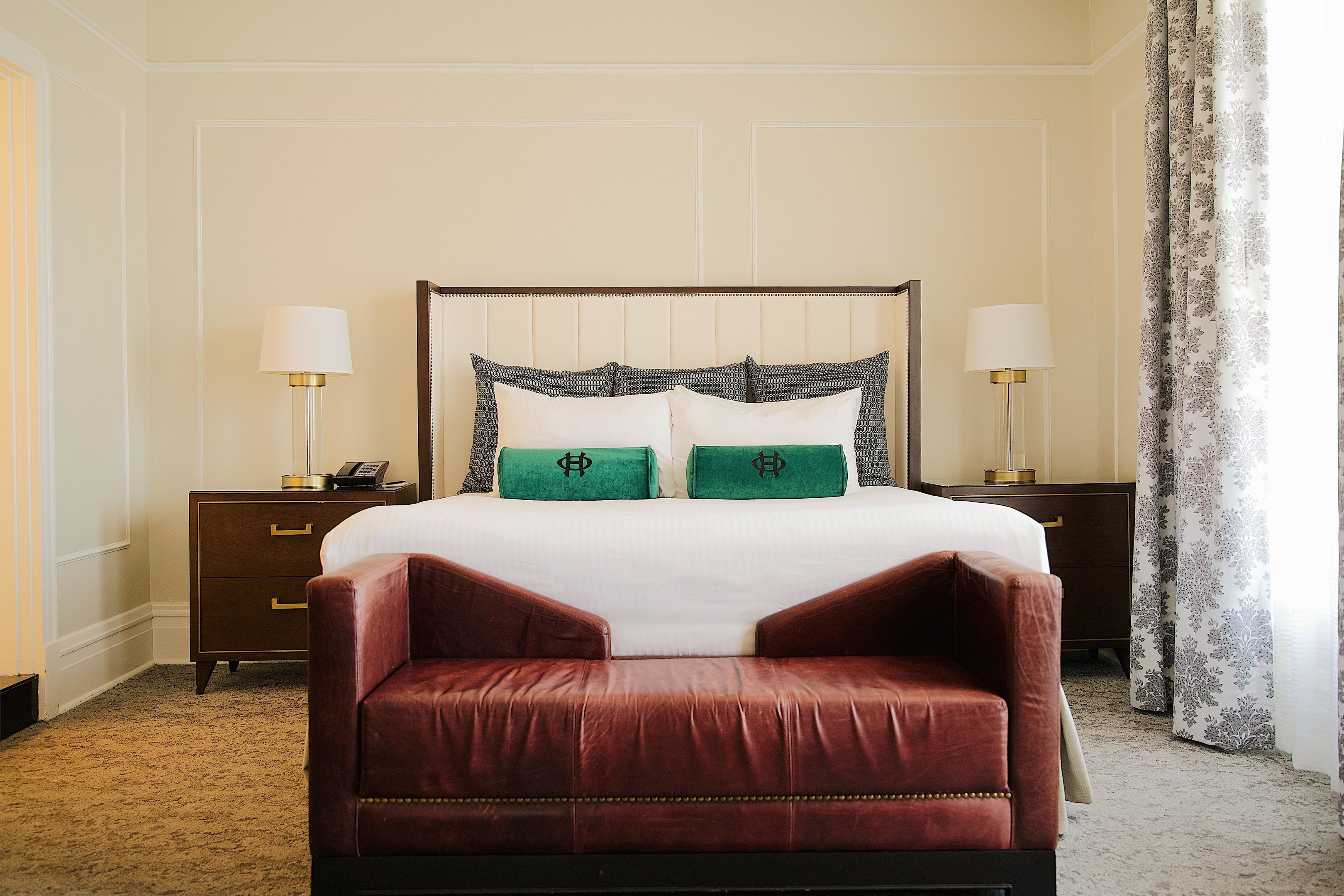 A hotel room with a large bed, two bedside tables, a nightstand, a red leather chair, and a curtain.