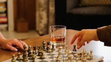 A chessboard with pieces and a glass of whiskey on a wooden table.