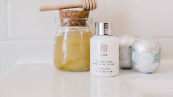 A bathroom counter with a glass jar of liquid, a bottle of lotion, and a bath product.