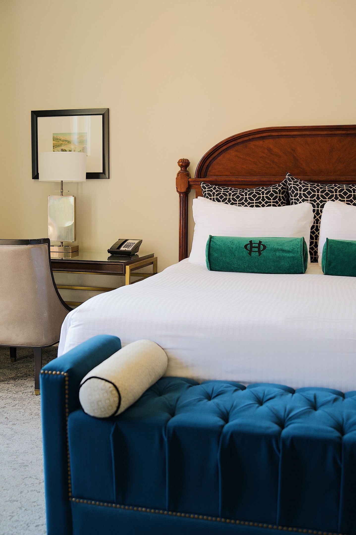 Habitación de hotel con cama, escritorio con teléfono, silla y un cuadro en la pared.