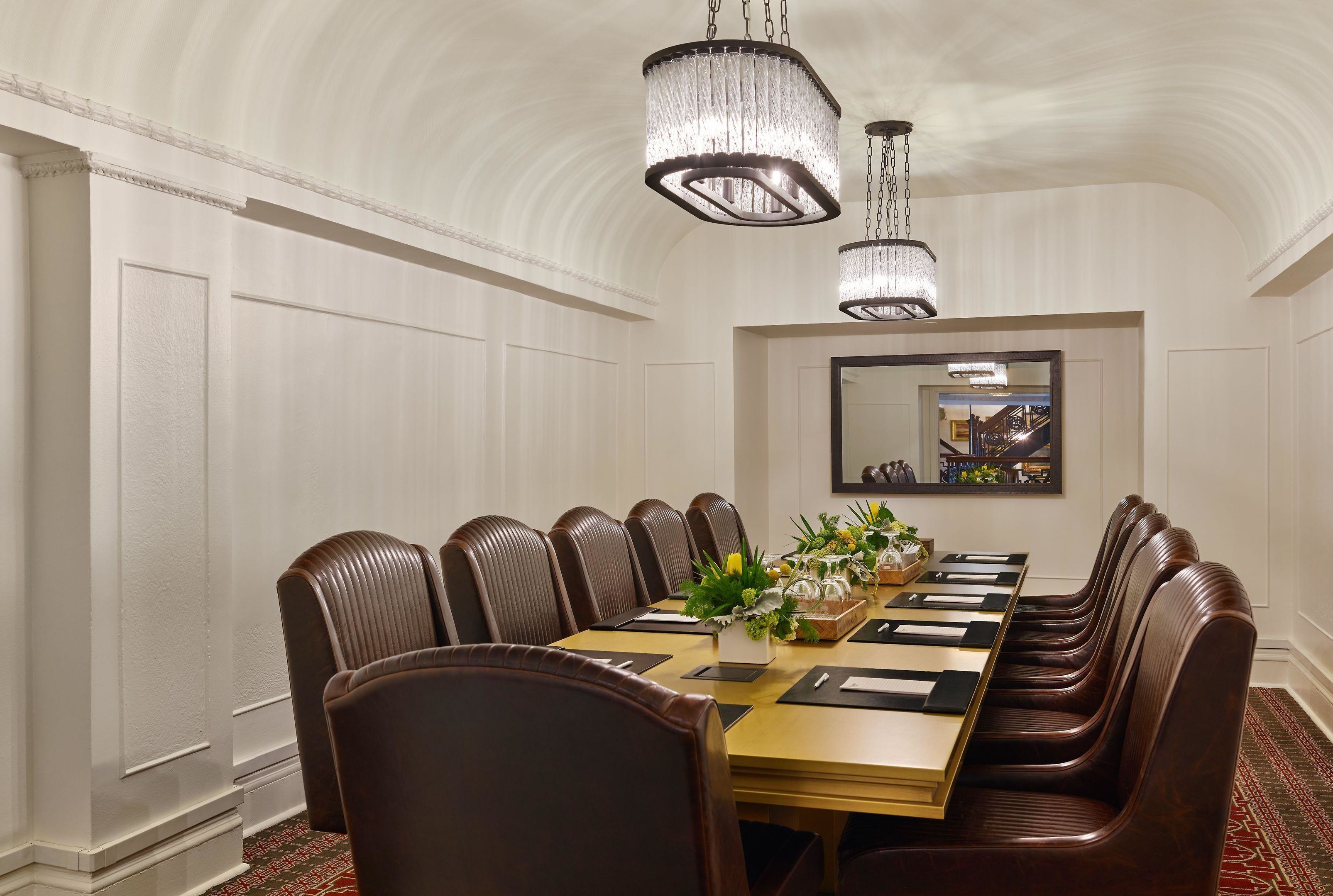 Un salón de conferencias con una mesa larga, sillas de cuero marrón y dos candelabros.
