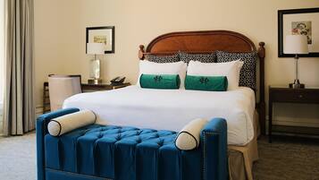 A hotel room with a bed, a blue upholstered bench, a nightstand with a lamp, and a framed picture on the wall.