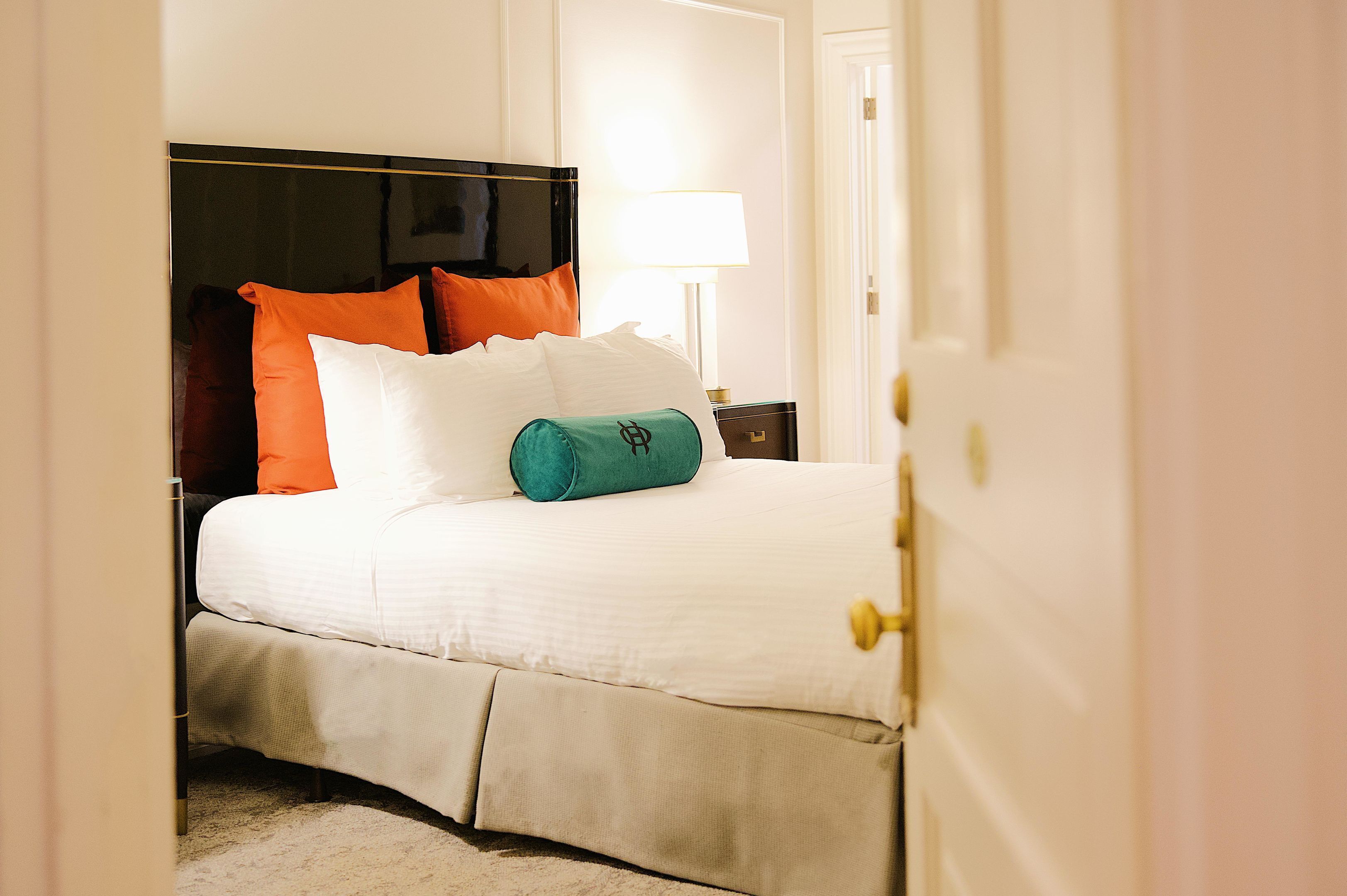 Un lit bien fait, avec une literie blanche, un coussin turquoise et des coussins orange.