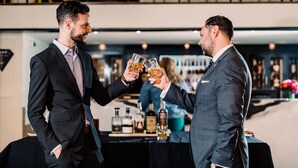 Two men in suits toasting with drinks at a bar with bottles in the background. - The Oxford Hotel (Denver)