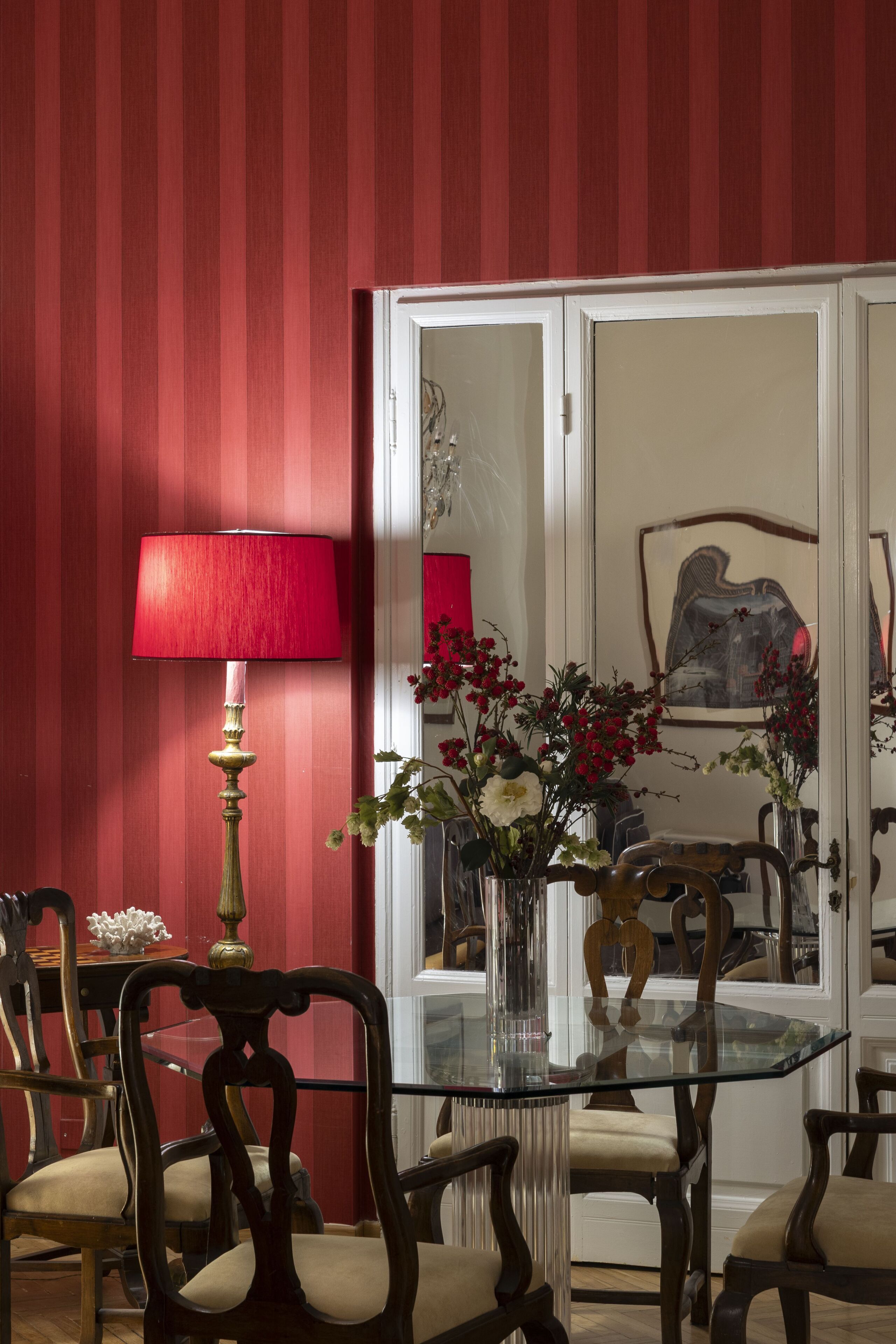 Un comedor con una mesa de vidrio rodeada de sillas de madera, una lámpara roja y un florero con flores.