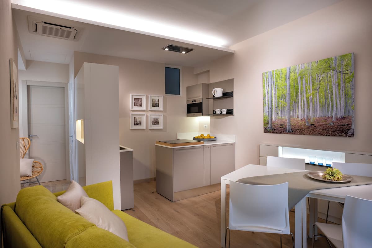 A modern kitchen with a dining area, a sofa, and a painting of a forest.