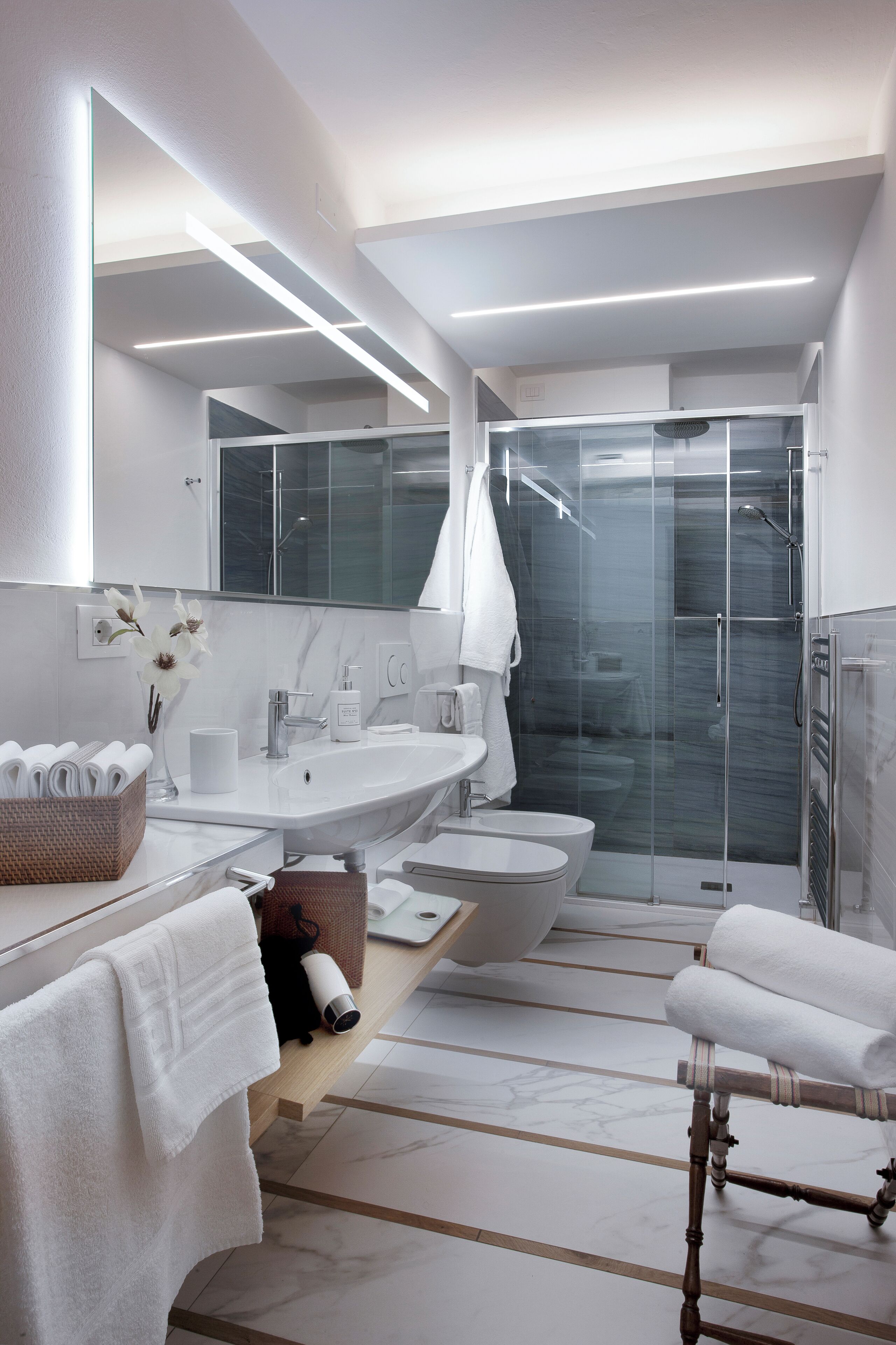 A modern bathroom with a large mirror, white fixtures, a glass shower enclosure, and a wooden vanity.