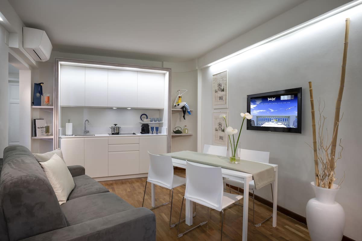A modern kitchen with white cabinets, a dining table with chairs, and a TV mounted on the wall.