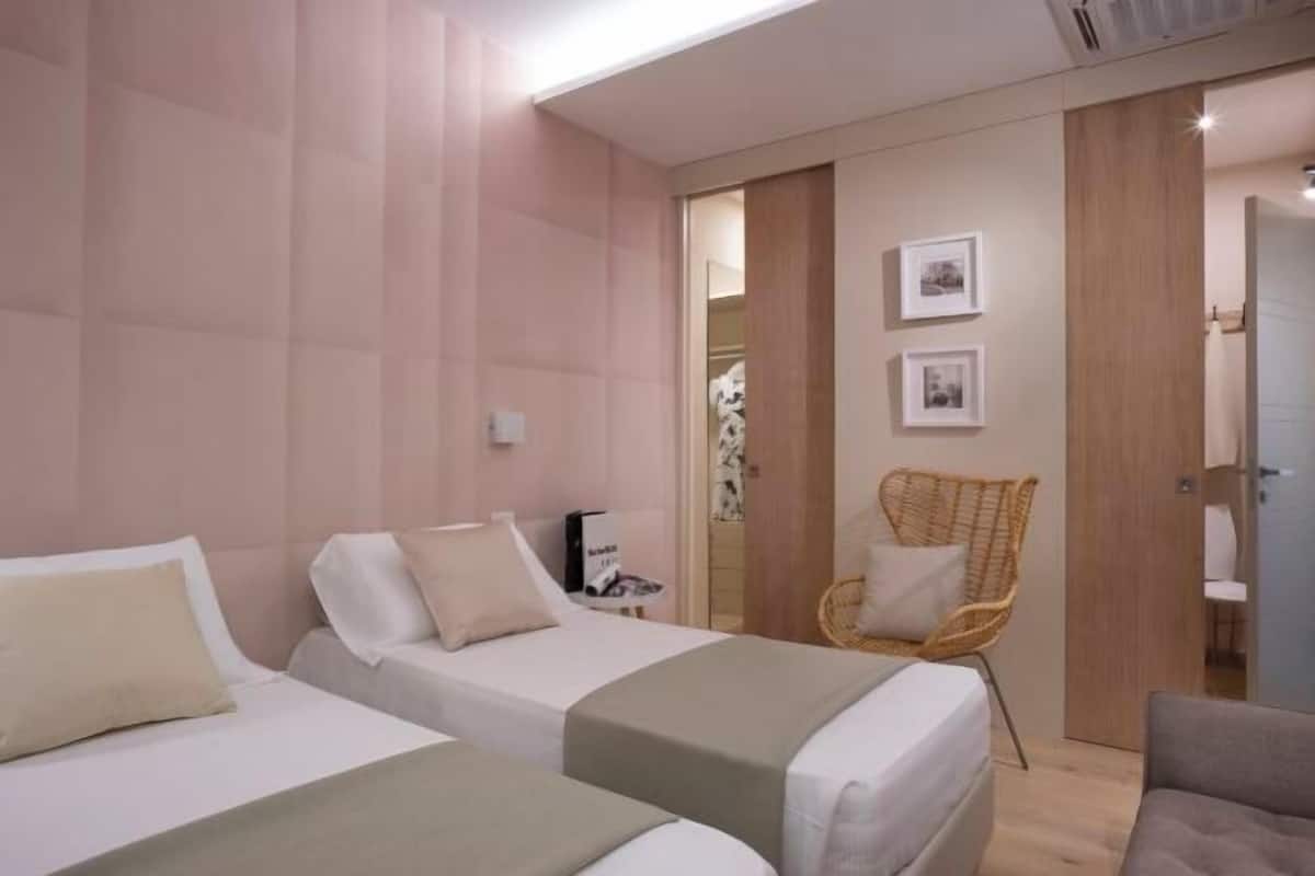 A hotel room with two beds, a wicker chair, and a wardrobe.