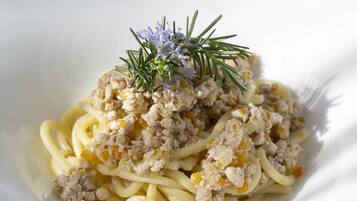 Un plato blanco con pasta, carne y una ramita de romero.