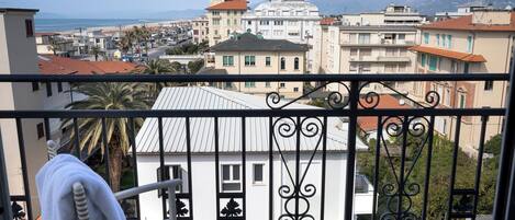 A balcony with a view of a coastal town, a chair, a table with a glass and a decorative item.
