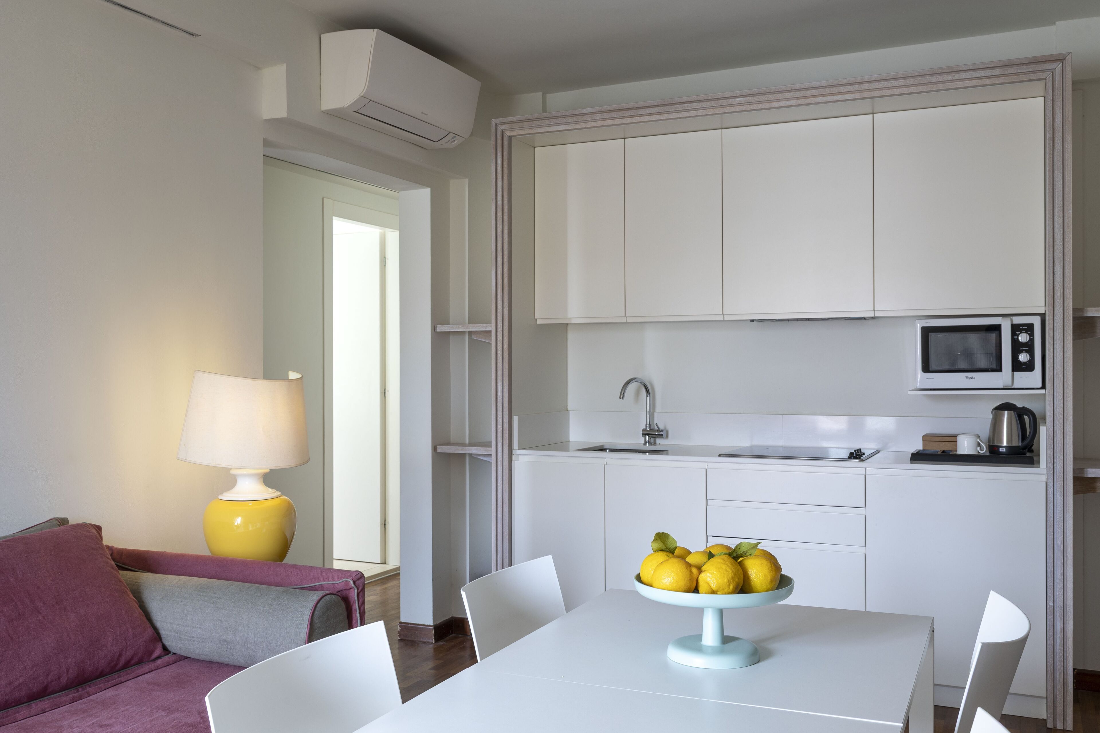 Una cocina moderna con armarios blancos, un microondas y un tazón de limones en la mesa de comedor.
