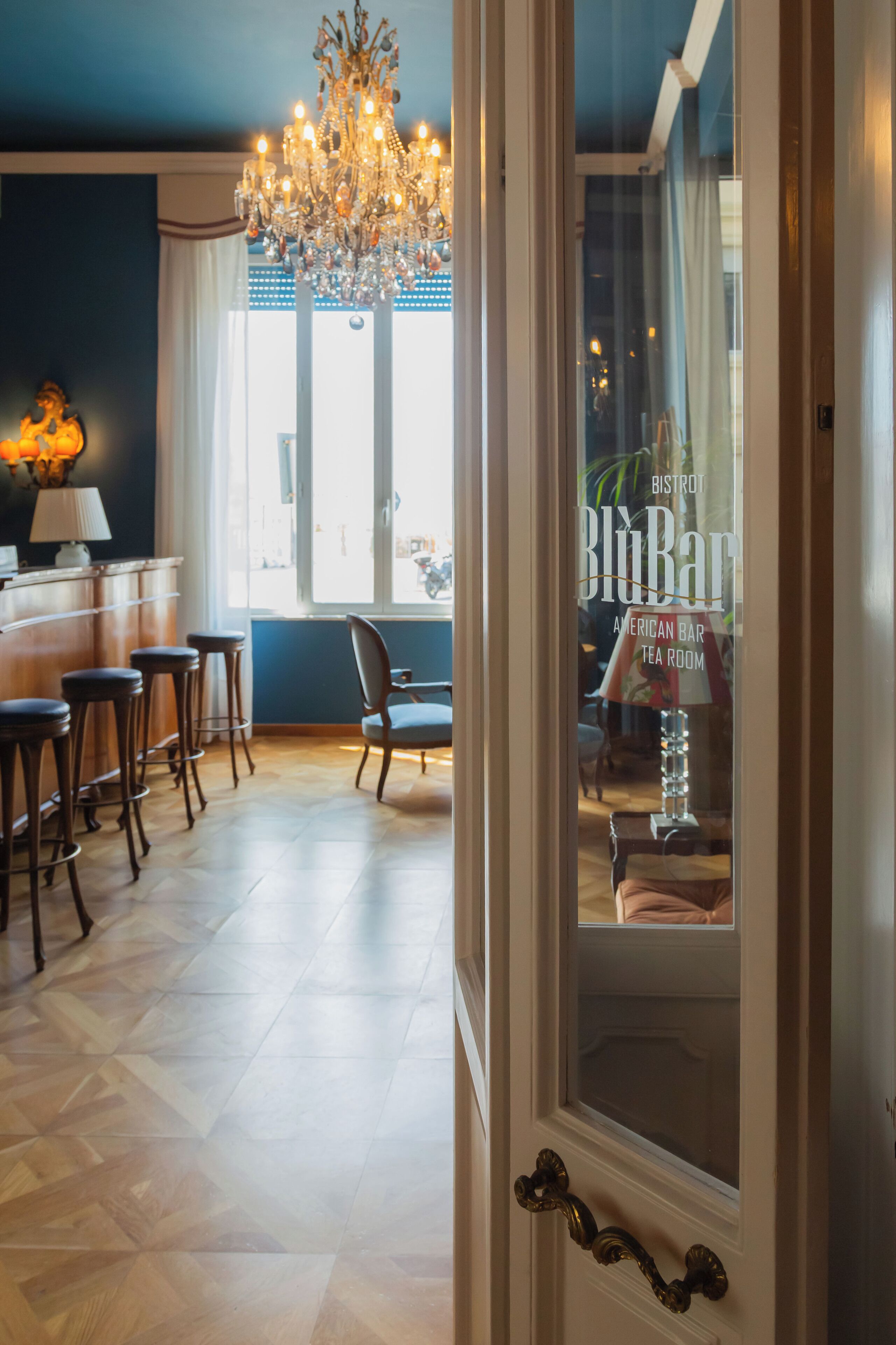 Uma área de bar com banquetas, um candelabro e vista para a rua através de uma janela.