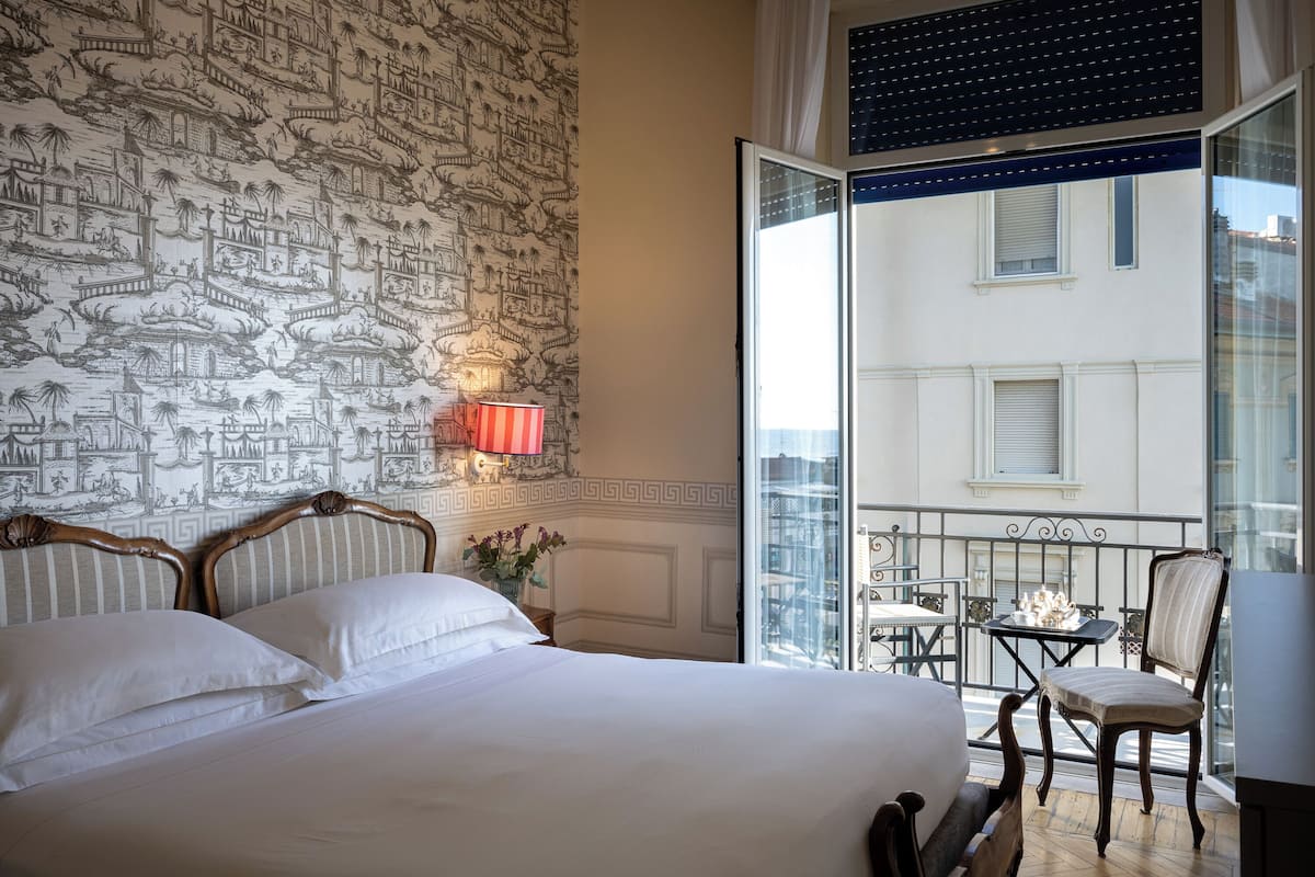 A hotel room with a large bed, a balcony with a table and chairs, and a view of the city.