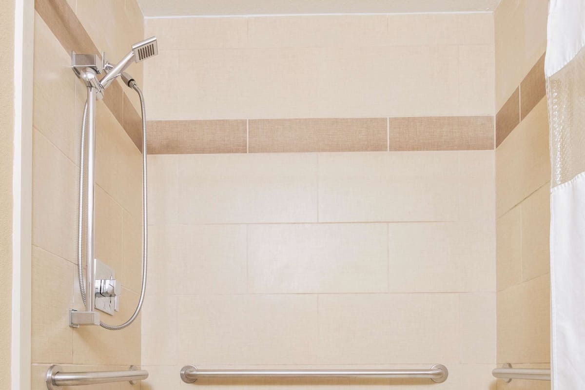 Un espacio de ducha pequeño y cerrado con una barra de apoyo, un cabezal de ducha y un banco blanco.
