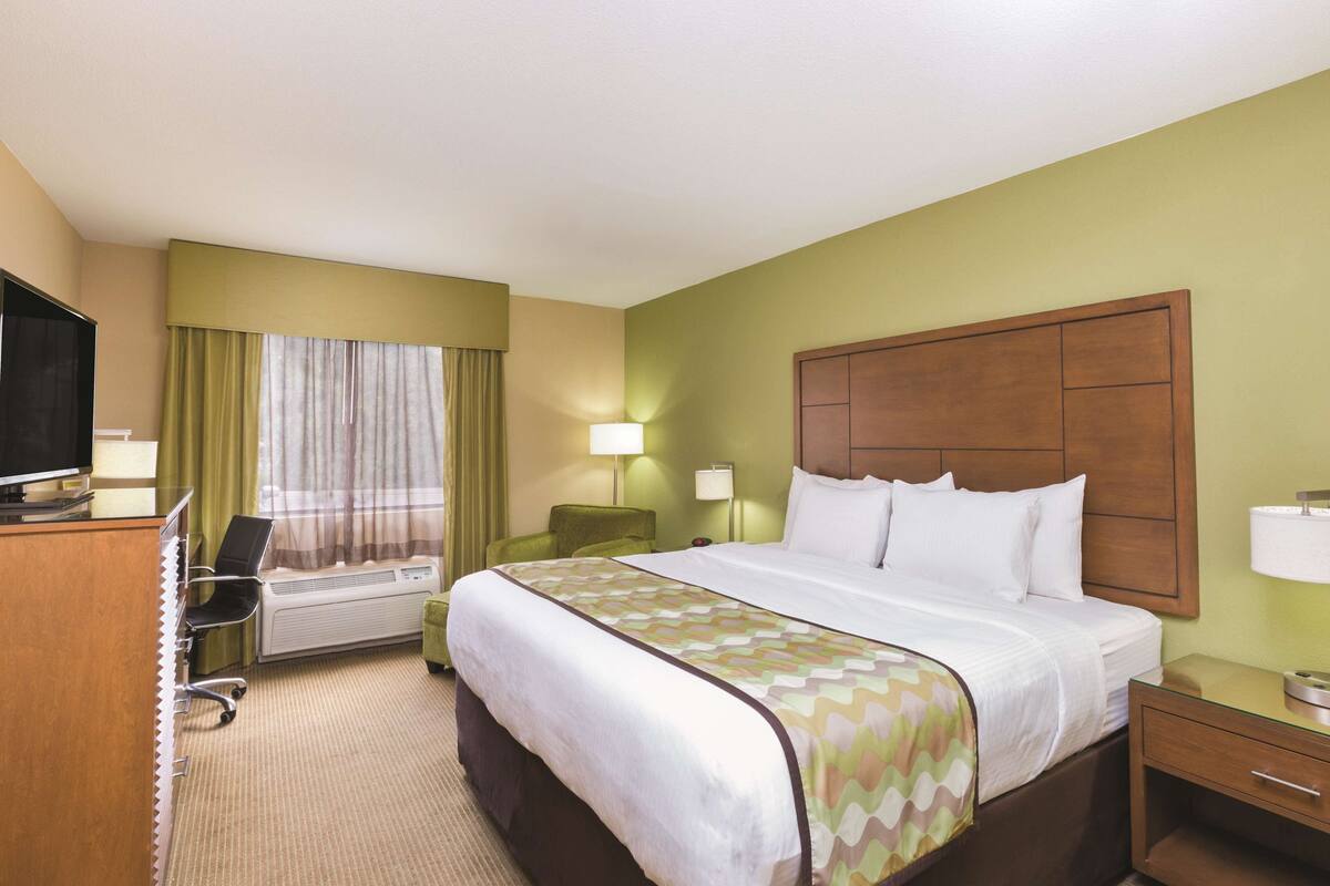Habitación de hotel con cama, escritorio con computadora, una silla, lámpara y televisor.