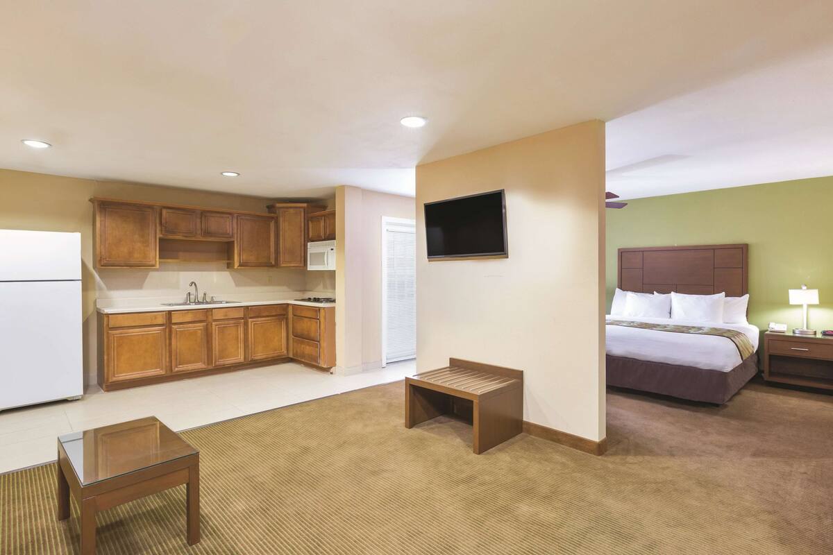 Una habitación de hotel pequeña con kitchenette, una cama, una mesita de noche y un televisor montado en la pared.