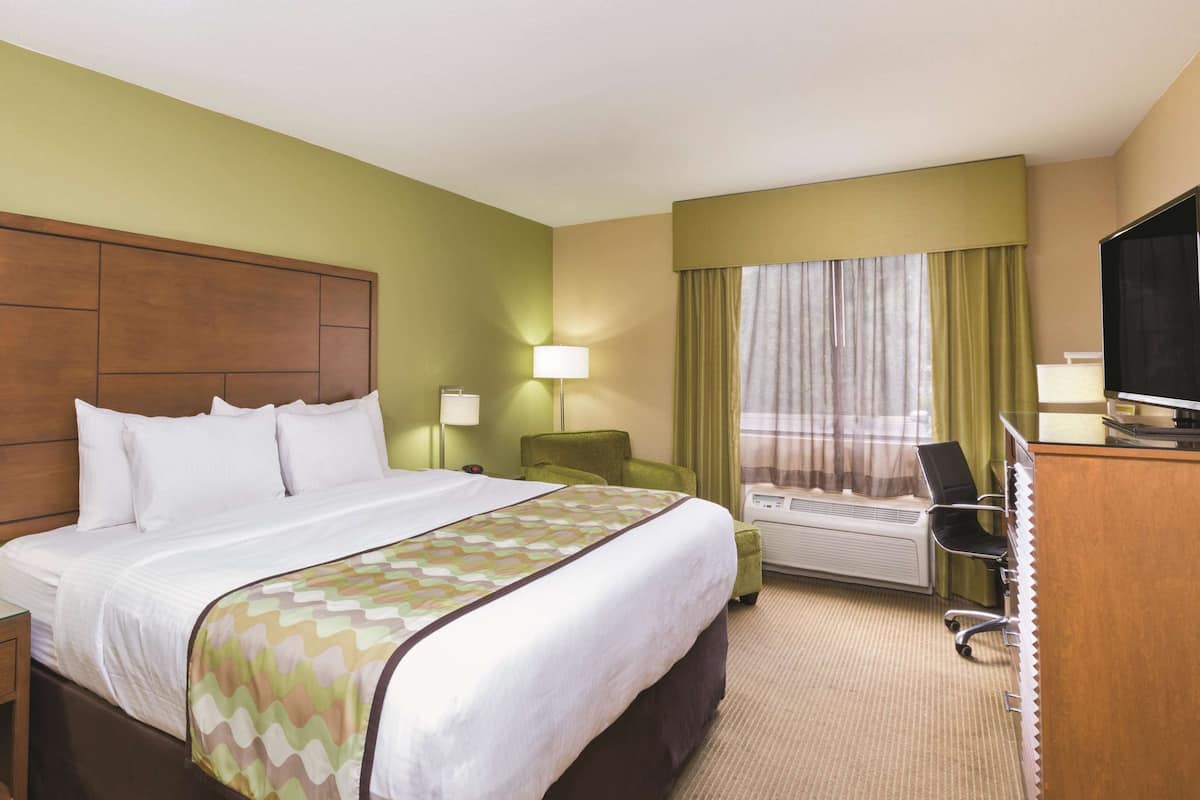 Una habitación de hotel con una cama grande, un escritorio con silla, televisión y ventana con cortinas.