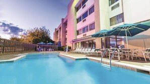 A swimming pool with lounge chairs and umbrellas, surrounded by a building with multiple floors and windows. - La Quinta Inn by Wyndham Austin North (Austin)