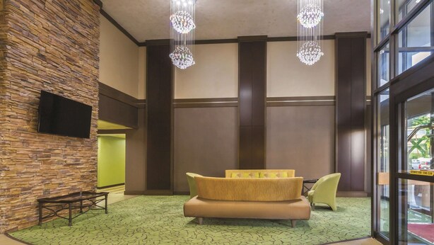 A lobby with a stone wall, a sofa, a bench, and a television. - La Quinta Inn by Wyndham Austin North (Austin)