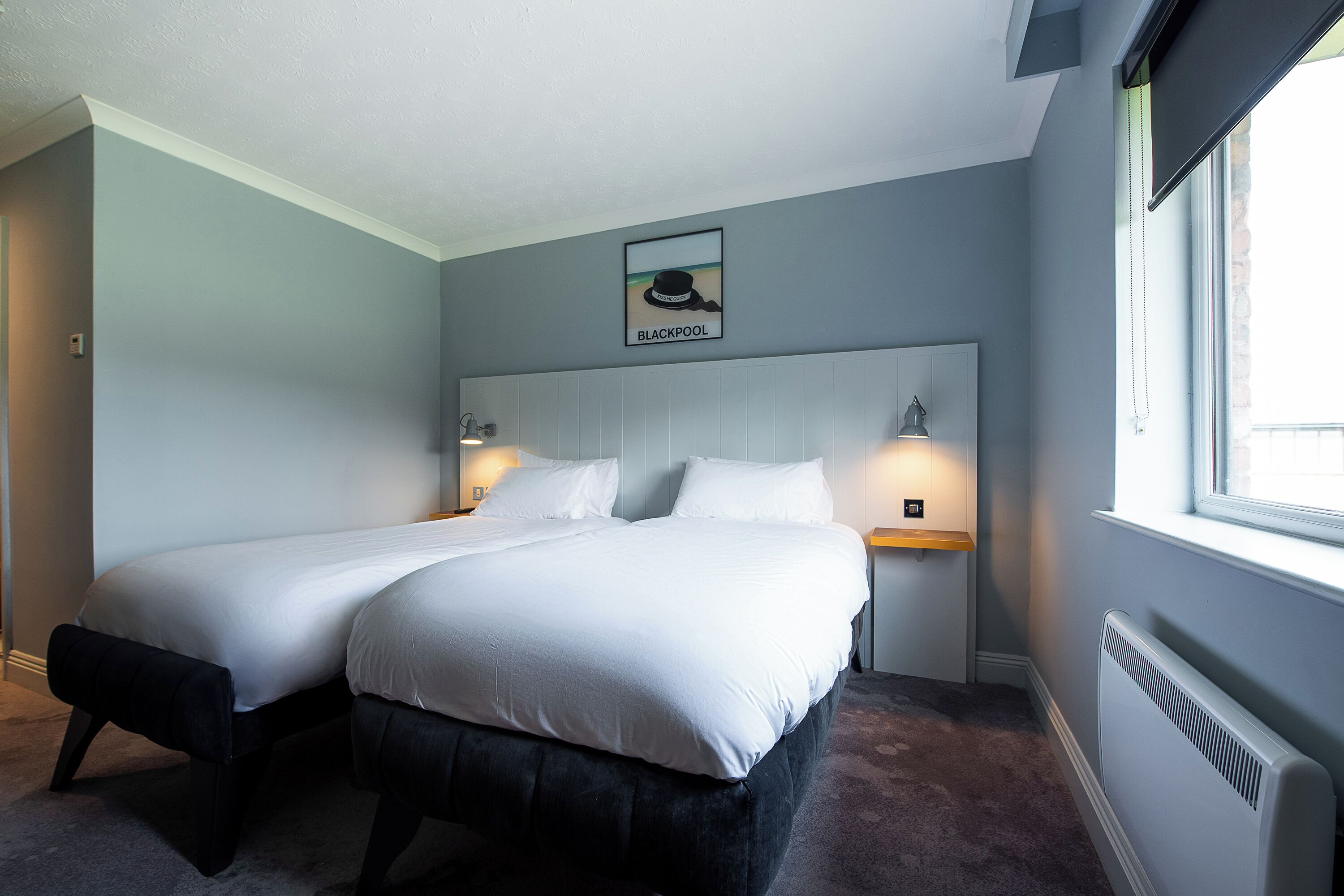 A hotel room with two beds, a framed picture of a hat on the wall, and a window with a view.
