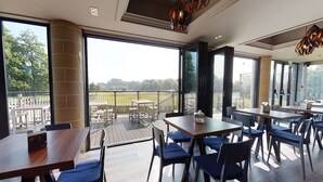 Un restaurante con terraza, amplias ventanas y vistas al campo.