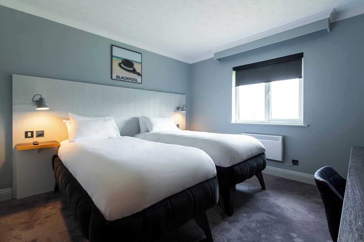 A hotel room with two beds, a headboard, bedside lamps, a window, and a radiator.