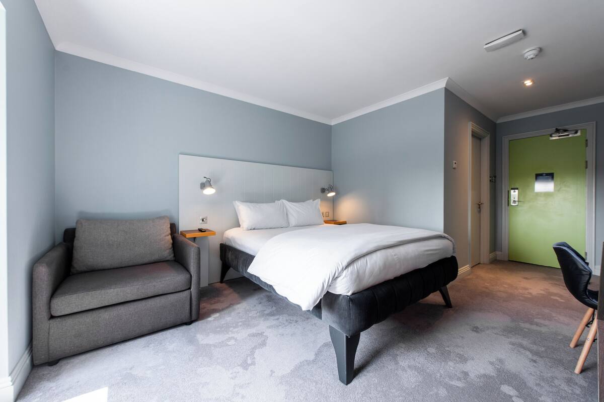 A modern bedroom with a bed, a sofa, and a chair.