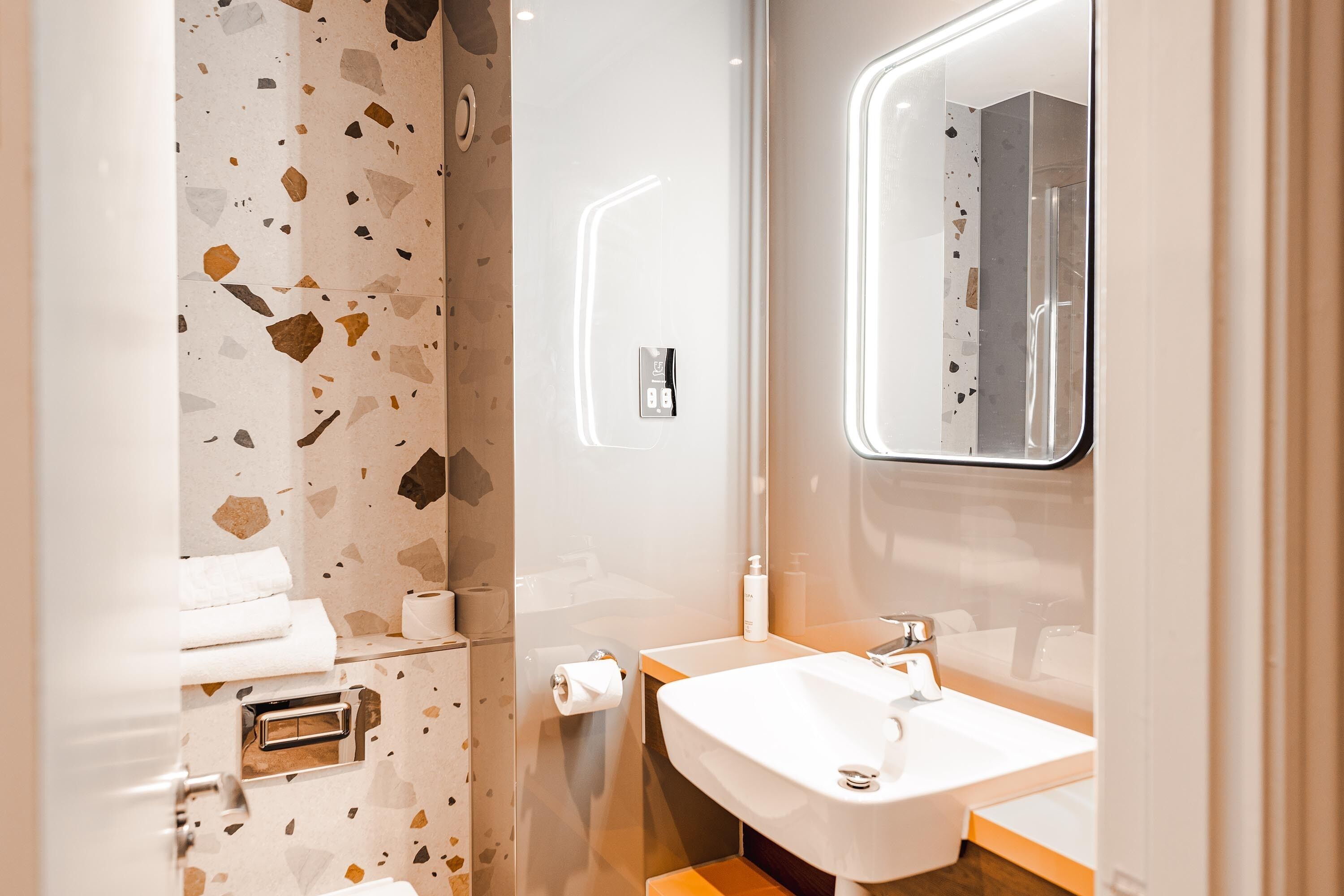 Un baño moderno con piso de terrazzo, un lavamanos blanco y un espejo encima.
