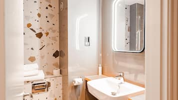 A modern bathroom with a terrazzo floor, a white sink, and a mirror above it.