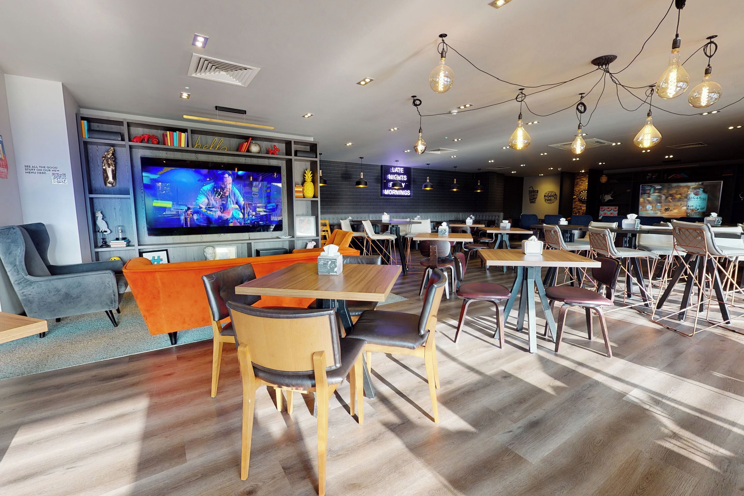 Ein modernes Restaurant mit großem Bildschirm, Holztischen und -stühlen.