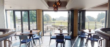 A spacious dining area with large windows, modern furniture, and a view of the outdoors.