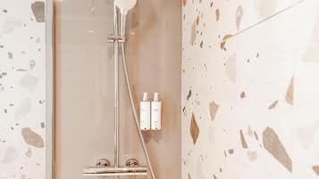 Ein modernes Badezimmer mit einer gläsernen Duschkabine, einer Handbrause und zwei Shampooflaschen an der Wand.