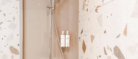 Un baño moderno con ducha acristalada, cabezal de ducha manual y dos botellas de champú en la pared.