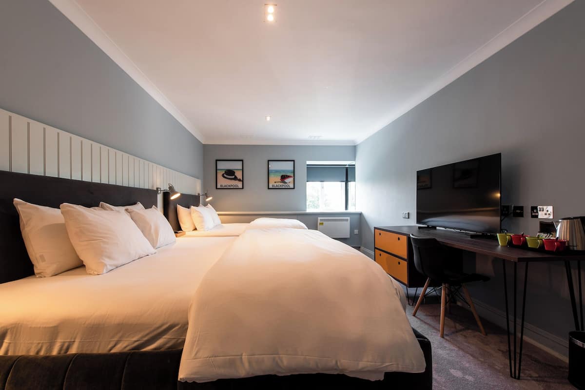 A hotel room with a large bed, a desk with a chair, a television, and a window.