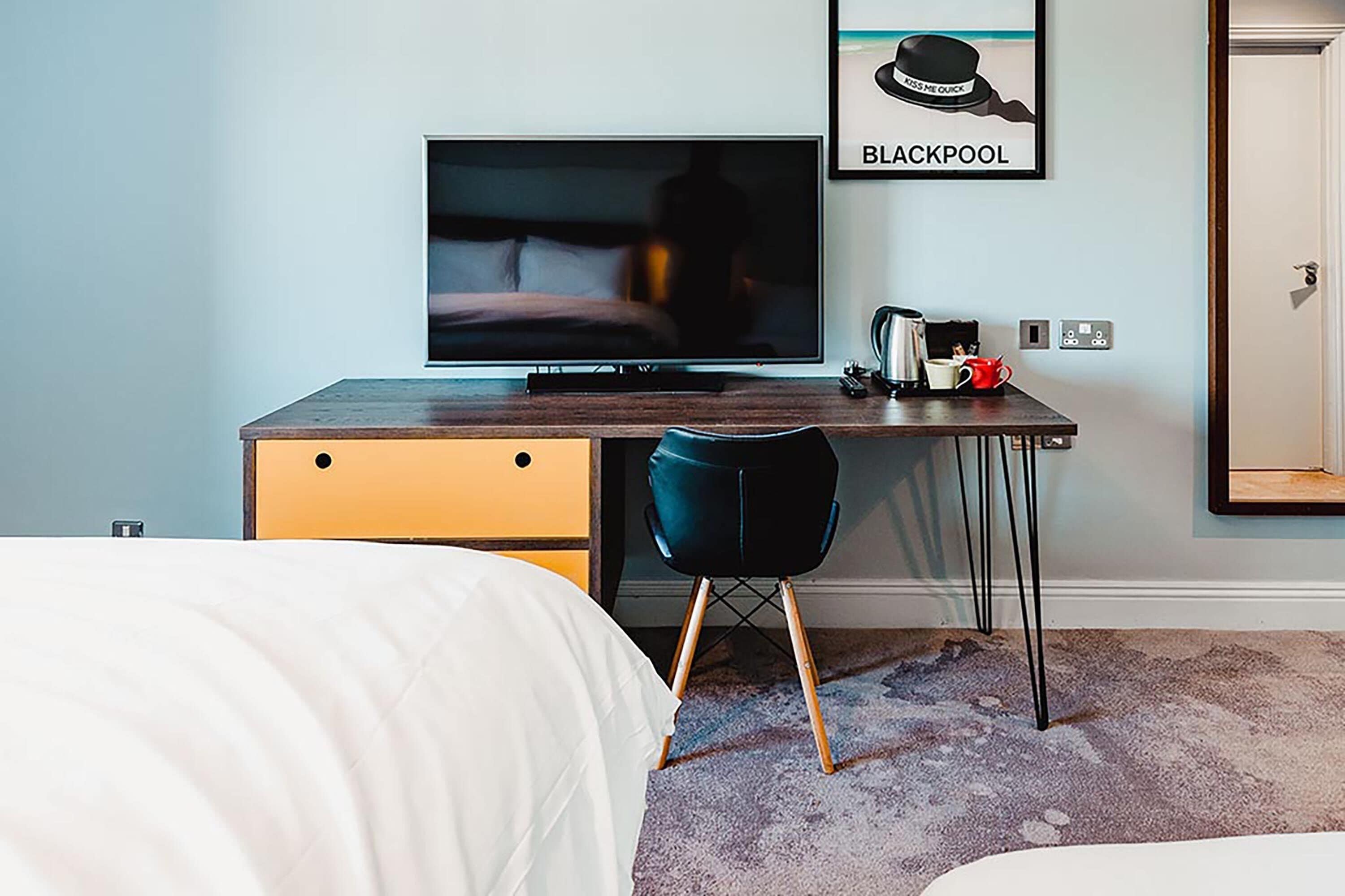 Ein Hotelzimmer mit einem Bett, einem Schreibtisch mit Fernseher, einem Sessel und einem gerahmten Bild an der Wand.