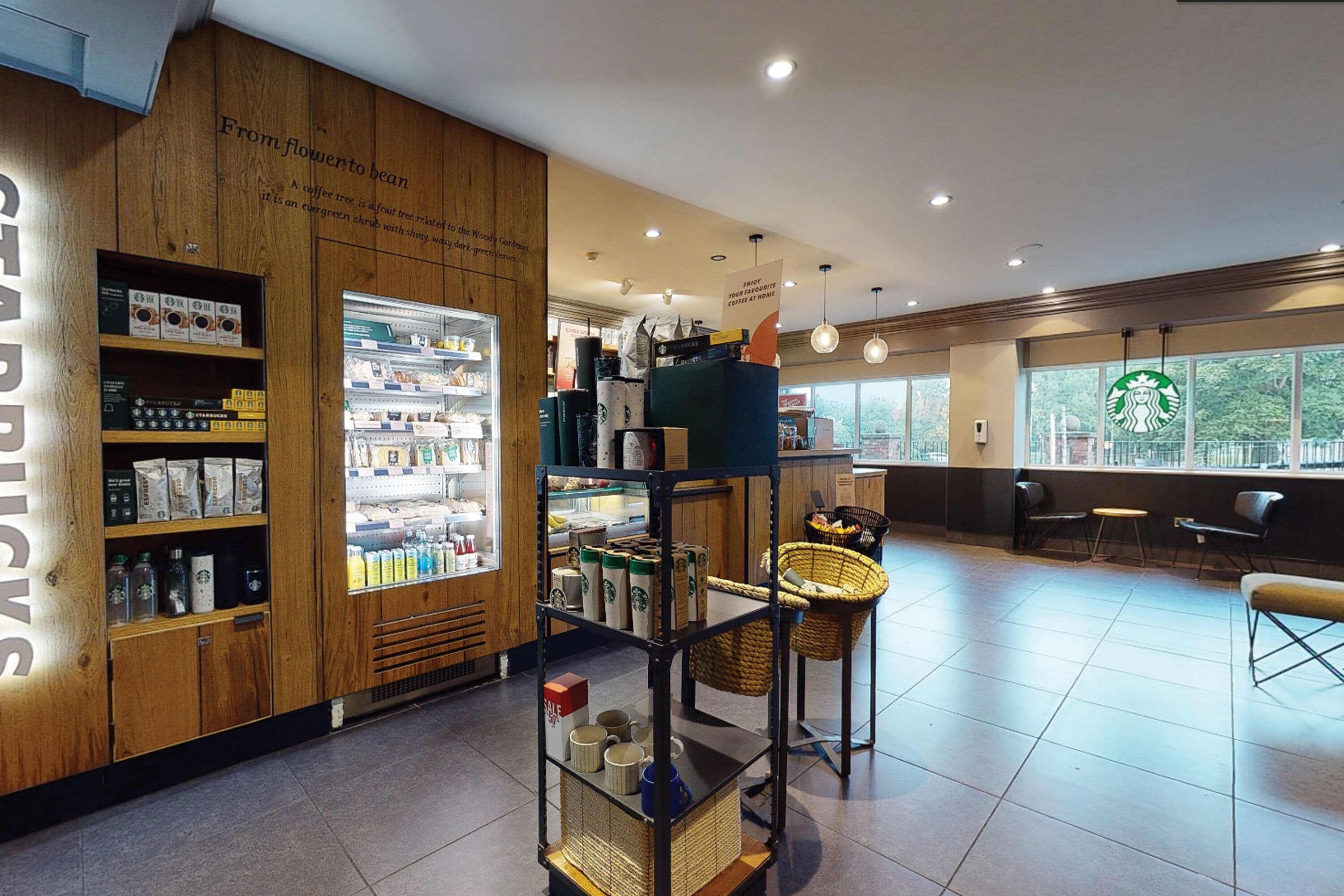A Starbucks store interior with wooden accents, a refrigerated display, seating area, and a view through large windows.