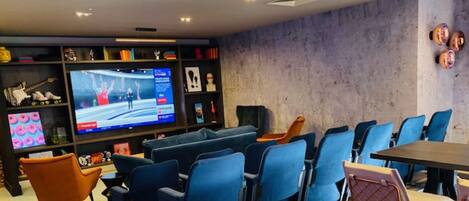 Una sala de cine moderna con asientos azules, una pantalla grande y diversas opciones de entretenimiento.
