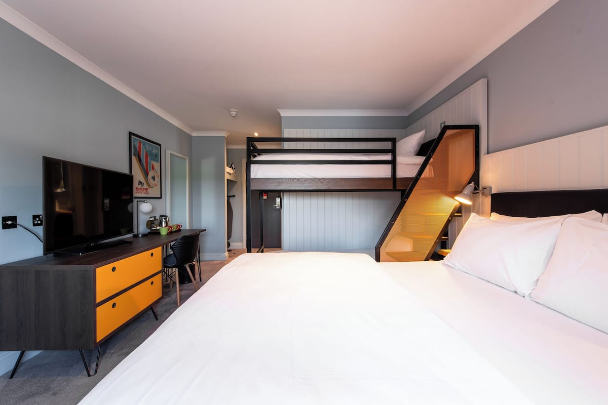 A modern hotel room with a bunk bed, a desk with a chair, a television, and a framed picture on the wall.