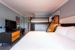 A modern hotel room with a bunk bed, a desk with a chair, a television, and a framed picture on the wall.