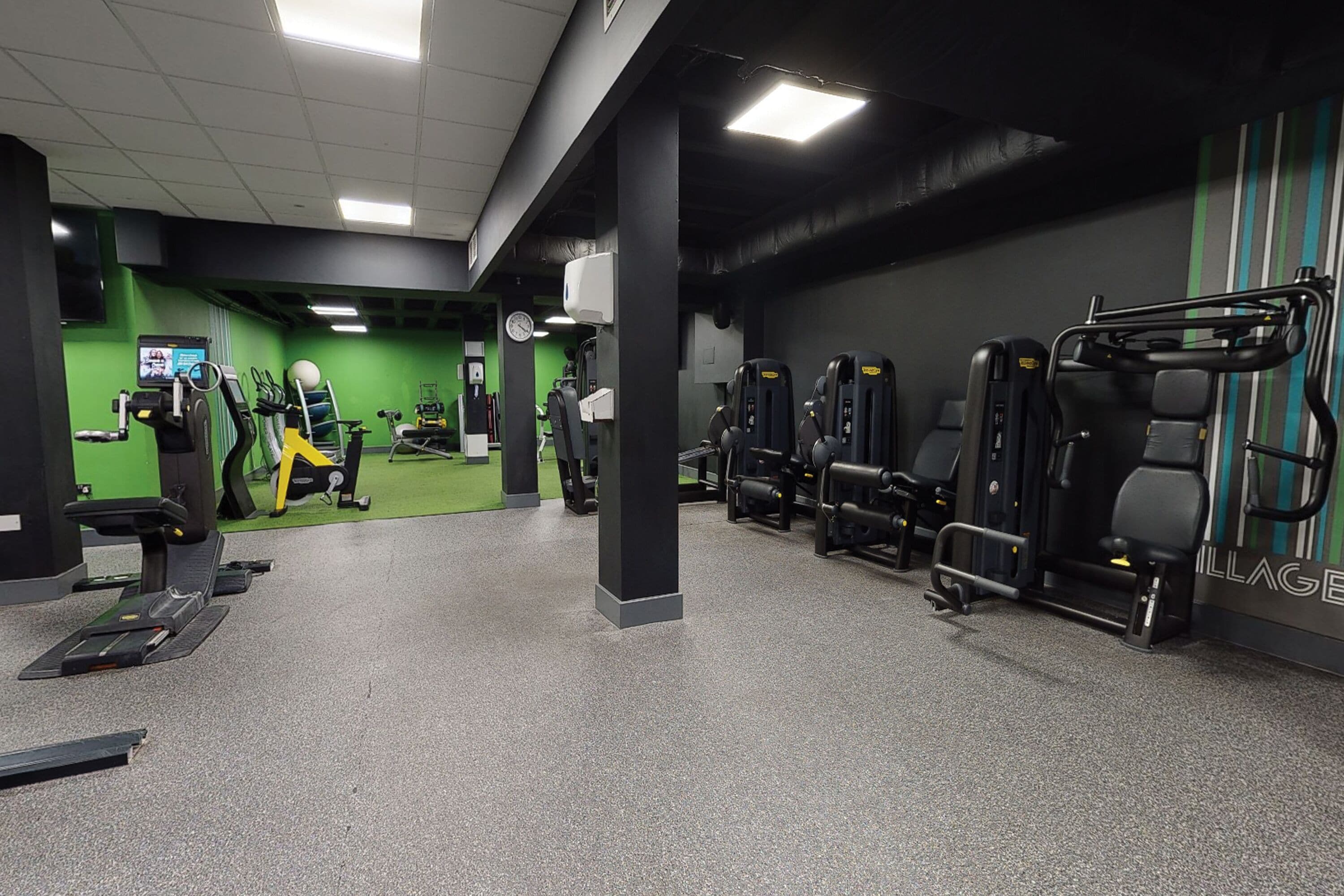 A gym with various exercise machines, a green wall, and a clock.