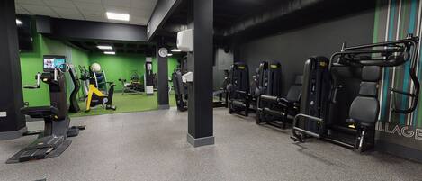 A gym with various exercise machines, a green wall, and a clock.
