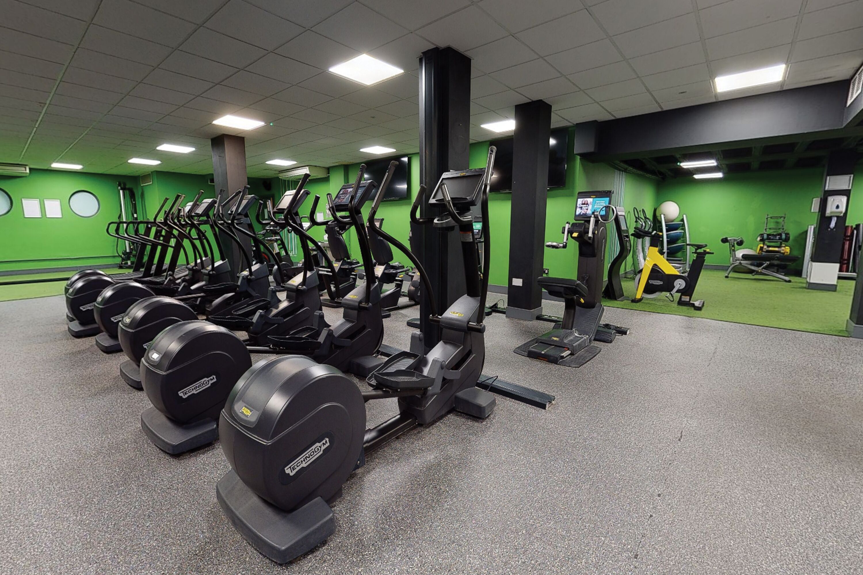 A gym with various exercise equipment, including treadmills and weight machines, arranged in rows.